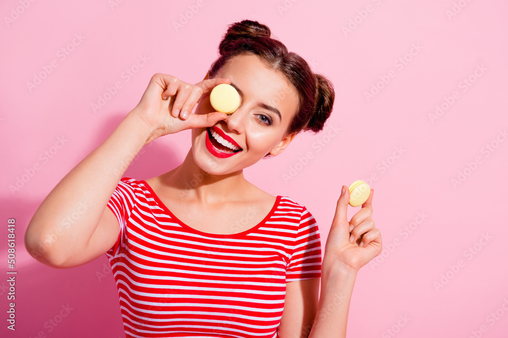 Poster photo of excited carefree girl hold macaroons cover eye have good mood isolated on pink color backgr