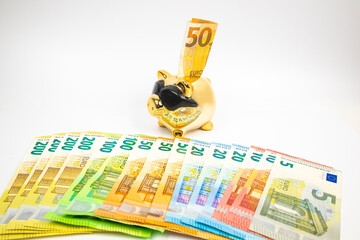 A golden piggy bank, 50 euros sticks out in it, euros, different banknotes lie nearby. The concept...