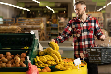 male shopper in the fruit section of the supermarket, man buying bananas in the grocery store, organic fruits, shopping