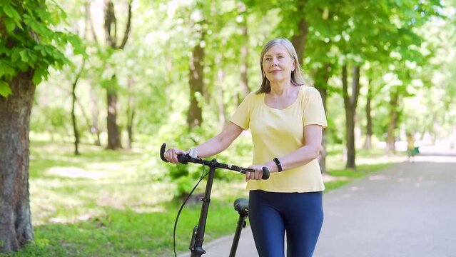 Happy senior mature modern active woman walks by bicycle on city urban park enjoys. Older female healthy lifestyle, free leisure time in retirement in bike. outdoors , walks in the fresh air in nature