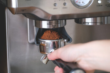 Hand holds a metal filter holder with grinded coffee beans in a coffee machine close-up, making...