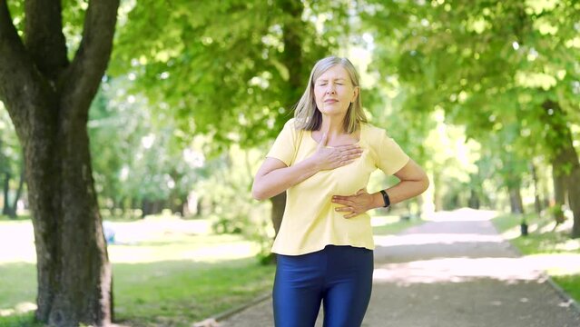 Senior eldery retired woman having heart pain while jogging heart attack. Mature female on a workout while running outdoors. suffers from chest hurt, ache. Old lady painful Outside on the city street