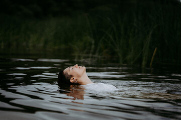 A young woman with a short haircut swims in a forest lake