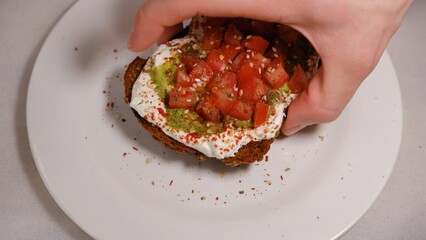Men's hand taking off Avocado sandwiches, half of avocado, with peanuts and pumpkin seeds, tomatos on a white background