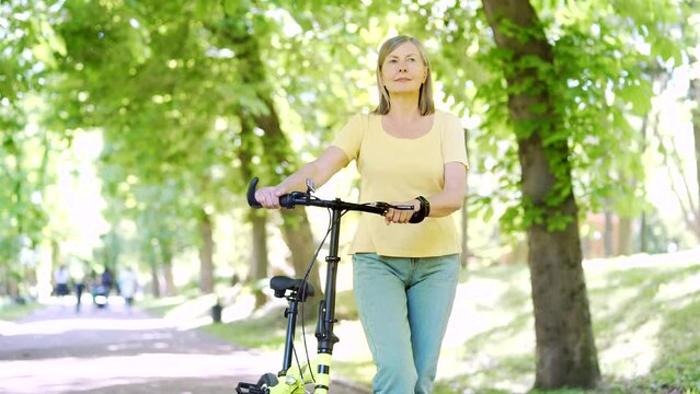 Happy senior mature modern active woman walks by bicycle on city urban park enjoys. Older female healthy lifestyle, free leisure time in retirement in bike. outdoors , walks in the fresh air in nature