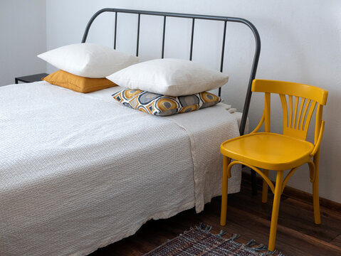 Simple interior with bed, chair and rug in white and yellow colors