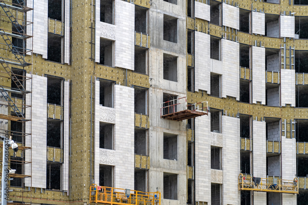 Poster monolithic concrete frame of apartment building under construction with partially attached facade cl