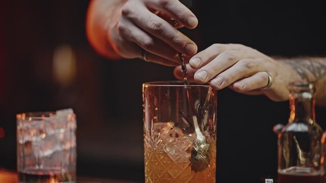 Experienced barman stirs orange cocktail with ice in glass