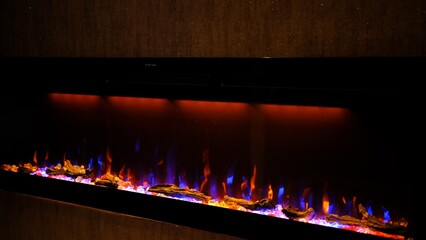 Side view on electric fireplace with artificial sparkling flame, decor for the interior, blue and...
