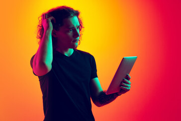 Emotive man, student with long curly hair using tablet isolated on gradient yellow-magenta...