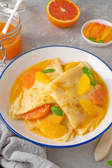 Delicious crepes suzette with orange syrup and slices fruits on a plate on a gray concrete background, top view