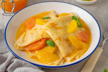 Delicious crepes suzette with orange syrup and slices fruits on a plate on a gray concrete background, top view