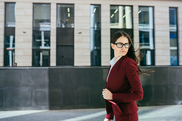 Dark haired confident businesswoman in a Burgundy pantsuit in a hurry walks to business center,...
