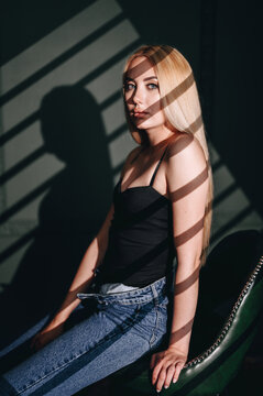 blonde with long hair is sitting on leather chair in black T-shirt. Studio light gobo mask