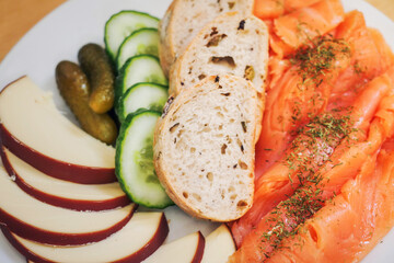 Close up of plate with smoked salmon, slices of bread, cornichons and cheese. Starter selection serving