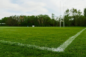 White line marking on a green field with tall goal post for hurling and camogie. National sport of Ireland. Blue cloudy sky. Irish national activity.