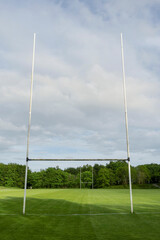 Green grass pitch with tall goal post for Irish National sport hurling and camogie. Popular game with ball and wooden stick. Blue cloudy sky. Vertical image.