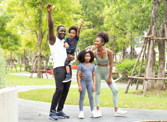 Happy family exercise in natural park. Black skin family, husband and wife have fun, laughing together with children at leisure in green garden. Playful kids have enjoyment outdoor with their parent 