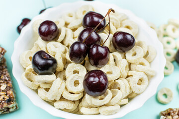 A bowl with oatmeal (corn) rings with cherry berries in close-up on a blue background. Dry healthy breakfast, add milk.