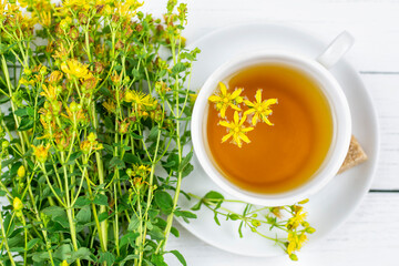 A drink (infusion, decoction) of St. John's wort in a white cup on a saucer on a white wooden background. Herb and flowers of the medicinal plant Hypericaceae, Hypericum.