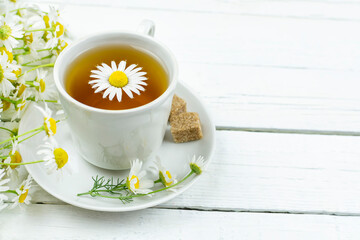 Tea (infusion, decoction) from chamomile medicinal (pharmacy) field in a cup on a saucer on a white wooden background. Space for the text. Medicinal herb Matricaria, herbal medicine.