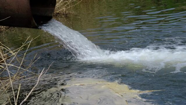 Draining sewage from pipe into river, pollution rivers and ecology.