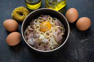 Carbonara pasta served with an egg yolk in a black bowl, studio shot on a dark-brown stone background