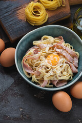 Green bowl with italian pasta carbonara over brown stone background, vertical shot, selective focus