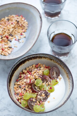Bowls with granola, greek yogurt and grapes, studio shot on a light-grey marble background with coffee glasses