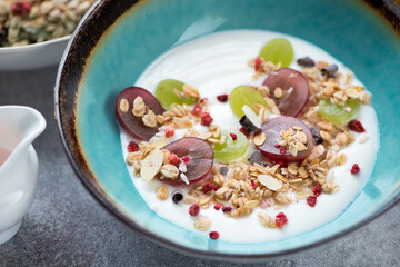 Turquoise bowl with greek yogurt, granola and sliced grapes, close-up, selective focus