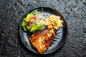 Meuniere of white fish tinned with tartar sauce and salad on a black plate against a black design board.