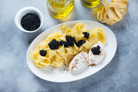 Pappardelle pasta served with black caviar and cheese, high angle view on a light-blue stone background, horizontal shot