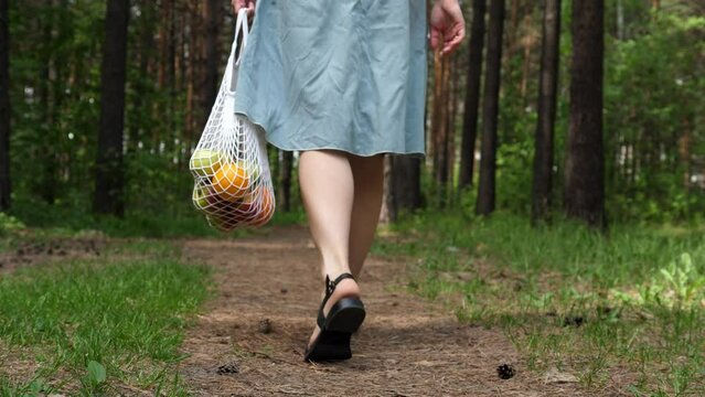 Woman walks with a braided string bag of fresh fruit. Life without plastic waste. Low-waste lifestyle. Sustainable ecological lifestyle