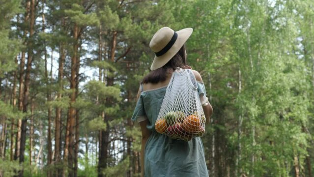 Woman walks with a braided string bag of fresh fruit. Life without plastic waste. Low-waste lifestyle. Sustainable ecological lifestyle