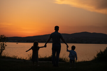 Fototapeta na wymiar dad with little son and daughter, holding hands in the summer and enjoying the sunset. Summer adventure, fun trip with kids. Fatherhood, Father's Day. Happy family travel and vacation concept.