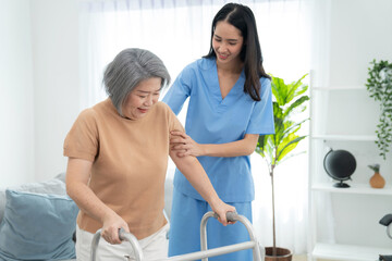 Fototapeta premium Elderly woman stand and walking with caregiver nurse at home. Attractive caregiver help to support arm. Senior patient do physical therapy and exercise muscle. Healthcare and lifestyle concept