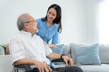 Obraz premium Attractive caregiver nurse stand behind elderly man who sitting on the wheelchair and smile at home. Doctor take care and encourage patient. Rehabilitation and healthcare concept