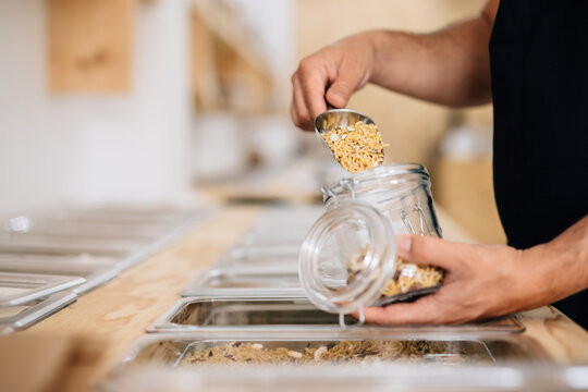 Woman putting dry pasta in glass jar in shop