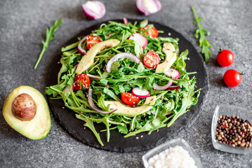 Vegan food. Healthy fresh vegetable salad - tomatoes, arugula, avocado, radish on a stone background. Diet menu.