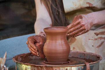 A pretty girl potters on a wheel. A ceramist creates a jug in the studio. Traditional pottery technique