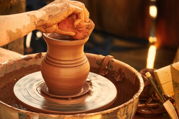 A pot on a potter's wheel illuminated by warm sunlight. The potter's hands turn a lump of clay into...