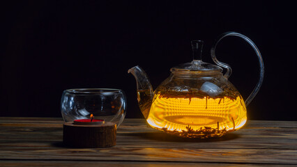 Hot herbal tea in glass teapot on wooden table on dark background. Traditional herbal drink. Place for text or design.