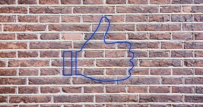 Image of glowing neon thumbs up icon on brick wall