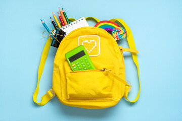 Back to school, education concept Yellow backpack with school supplies - notebook, pens, eraser rainbow, numbers isolated on blue background Top view Copy space Flat lay composition