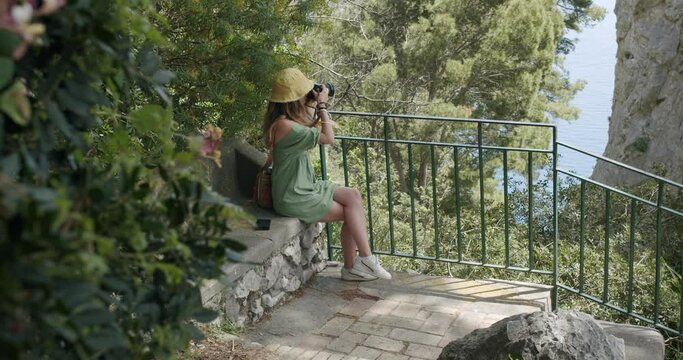 A young woman photographer takes a picture of the Natural Arch, one of the best touristic locations of Capri, in Italy - 02