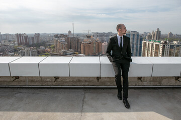 a man in a black suit with a tie sits on the roof against the backdrop of the panorama of the city
