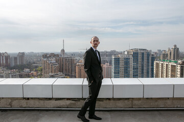 a man in a black suit with a tie stands on the roof against the backdrop of the panorama of the city