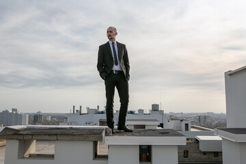 a man in a black suit with a tie stands on the roof and looks ahead
