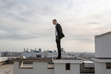 a man in a black suit with a tie stands on the roof and looks ahead