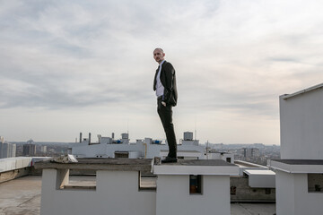 a man in a black suit with a tie stands on the roof and looks ahead